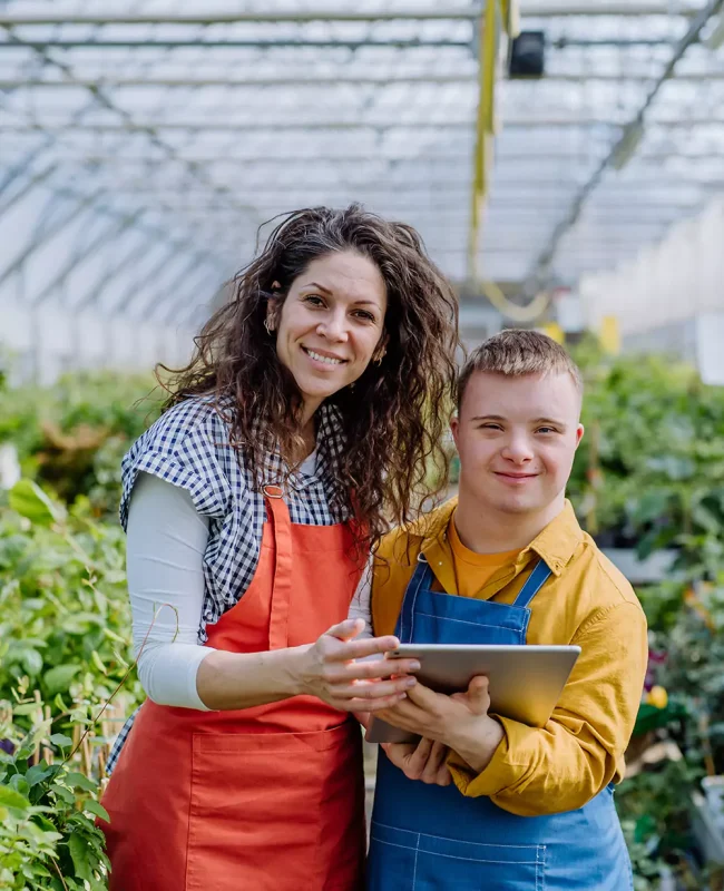 A down syndrome man and his carer working in a plant nursery outdoors