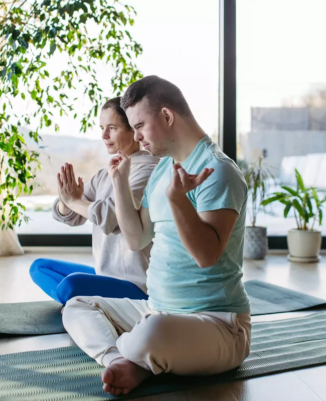 A down syndrome man doing yoga with his care giver